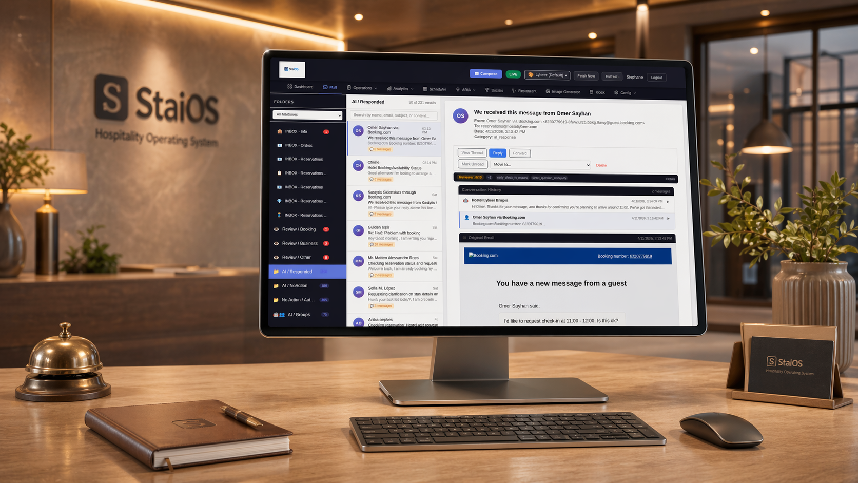 StaiOS mail agent open on a desktop monitor in a warm hotel back-office, showing a classified multilingual email thread